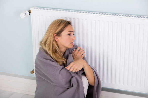 image of homeowner sitting by radiator depicting heating system not working