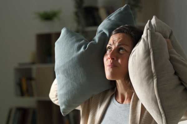 Woman covering ear with pillows due to loud AC compressor