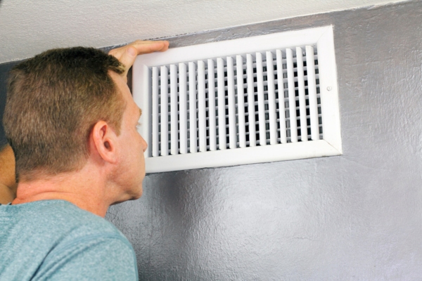 man inspecting home air vent due to rattling ductwork noise