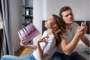 couple feeling warm and humid with girl using magazine as fan and guy checking air conditioner remote