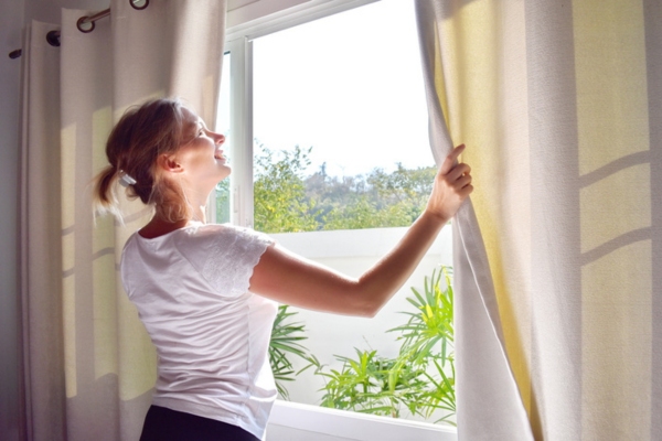 homeowner shutting curtains during summer to block the sun and avoid heat exhaustion