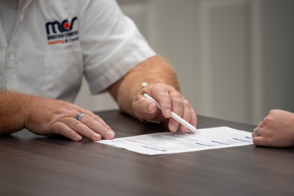 photo of a hand and checklist of a Modern Comfort staff explaining HVAC systems to a client