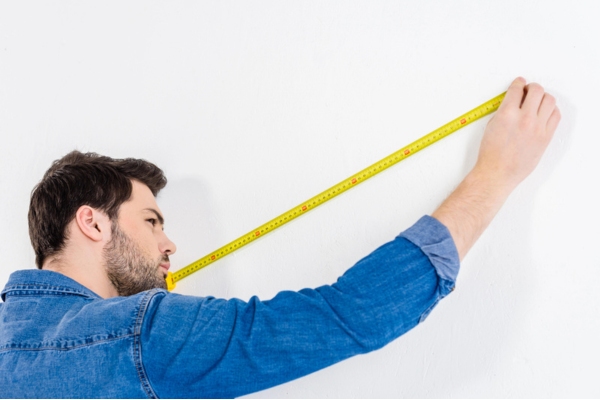 man using a tape measure against a white wall depicting furnace sizing