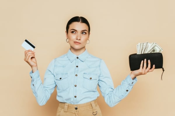 woman holding card and wallet with cash on each hand depicting cost considerations of furnace and heat pump