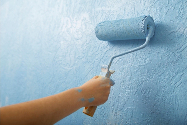 cropped hand of a woman painting the wall light blue depicting indoor air pollution