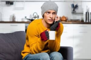 man feeling cold indoors while on a phone with a furnace repair company