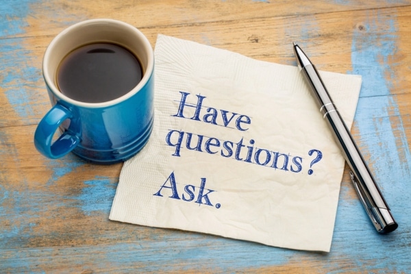 "have questions ask" written on a table napkin placed beside coffee and a pen depicting FAQs about furnace efficiency