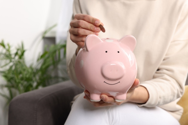 woman adding coin inside piggy bank depicting reduced energy consumption