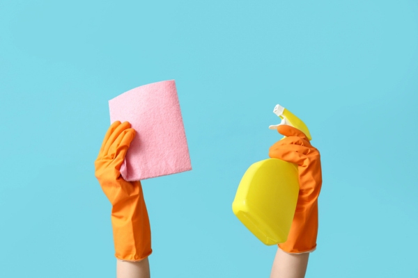 Female hands in rubber gloves holding rag and bottle spritzer depicting cleaning around furnace