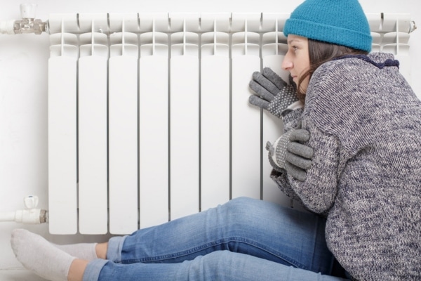 woman feeling cold sitting by the radiator at home depicting heating system not working efficiently