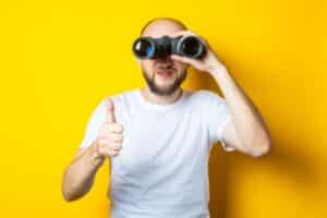 man with a beard looks through binoculars while doing a thumbs up depicting looking for HVAC contractor